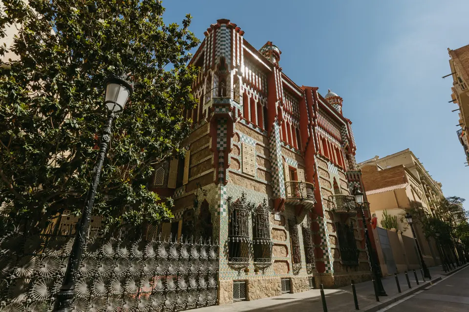 Angled street view of a stone and tile house, with a street lamp and a decorated metal fence