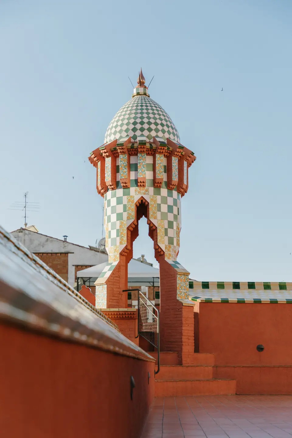 Cylindrical tower with a green and white checkered tiled dome above a terracotta rooftop wall