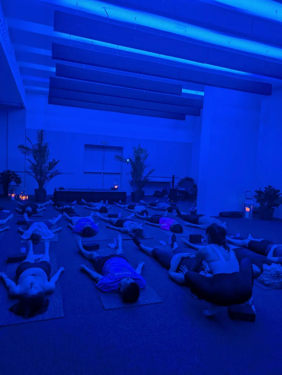 Dark room in deep blue light with people lying on mats and plants at the back