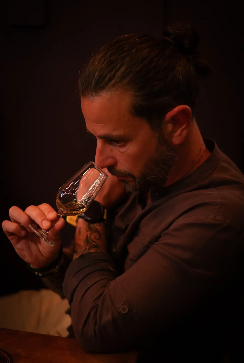 Man in profile nosing a whisky tasting glass in a dimly lit, warm room