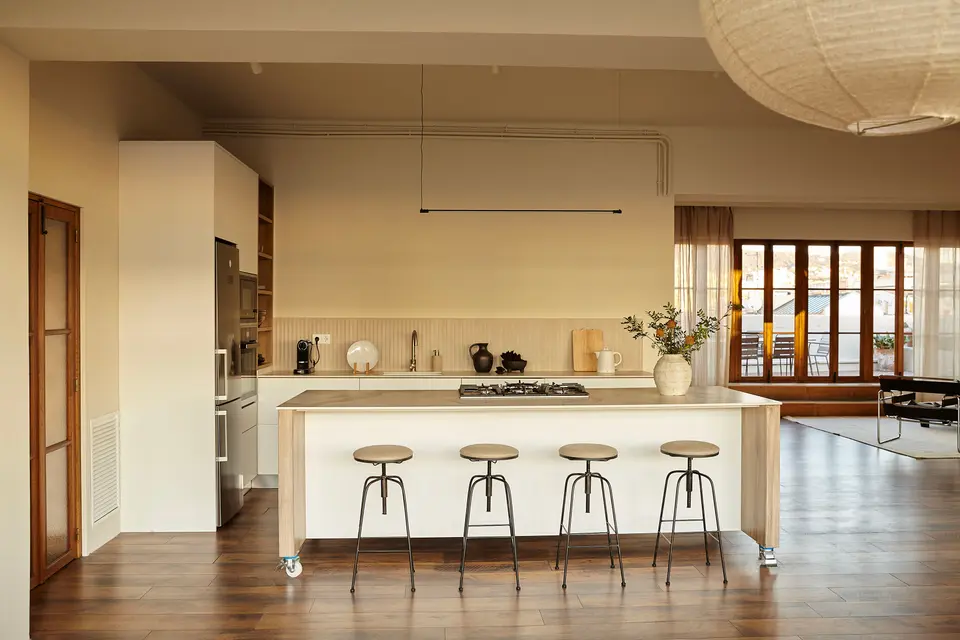 Light wood kitchen island with four stools on wheels, dark wood flooring and tall windows at the back
