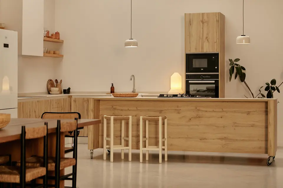 Kitchen with a light wood island on wheels and two stools, built-in oven and microwave, and a table with woven chairs