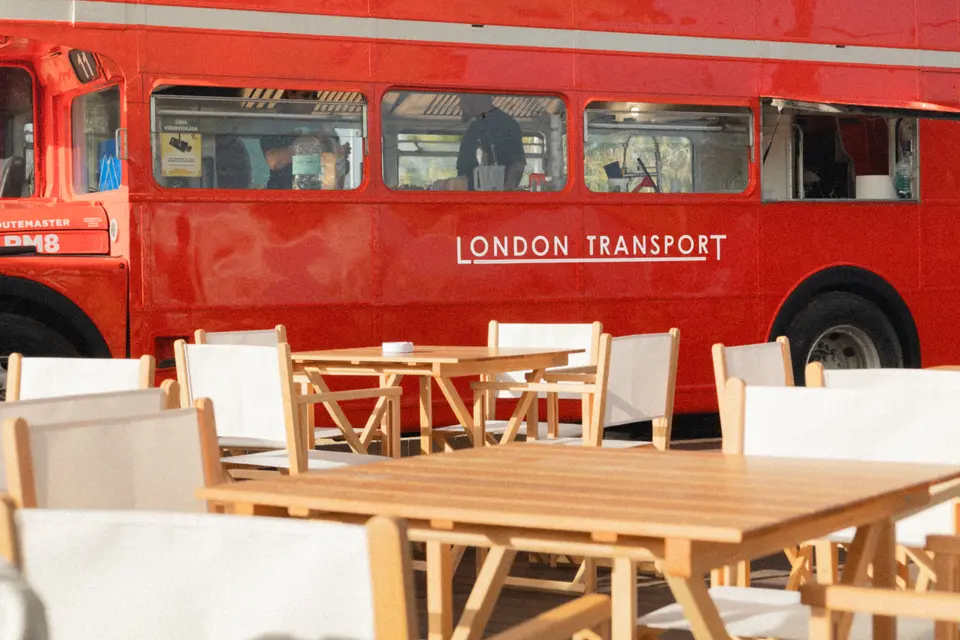 Side of the red English bus with the London Transport lettering, behind wooden tables and canvas folding chairs