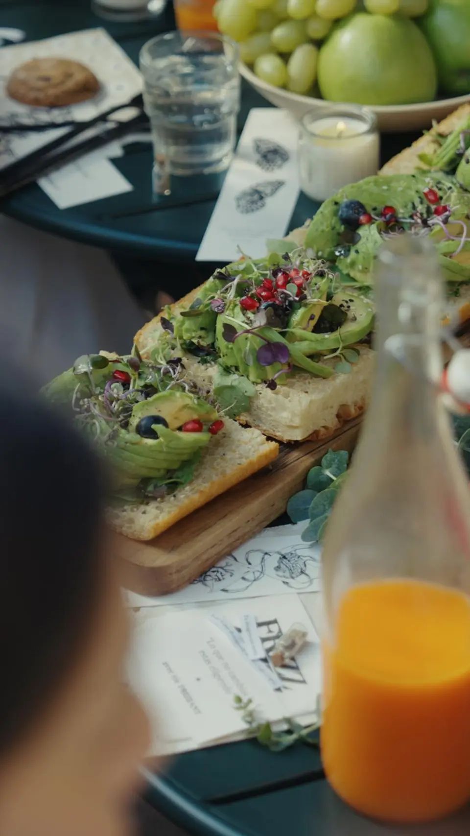 Board of avocado toasts topped with edible flowers beside a bottle of orange juice on the table