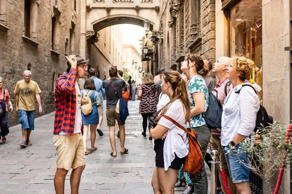 Group of people with backpacks on a narrow stone street looking up, with a covered bridge behind