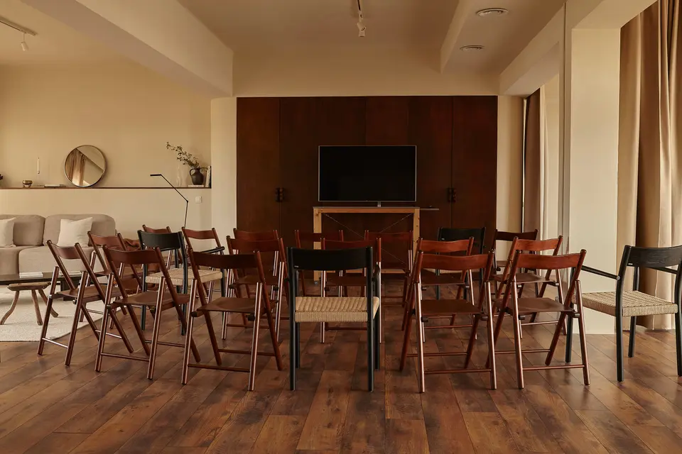 Wooden folding chairs in rows facing a TV screen, set up theatre-style on a parquet floor