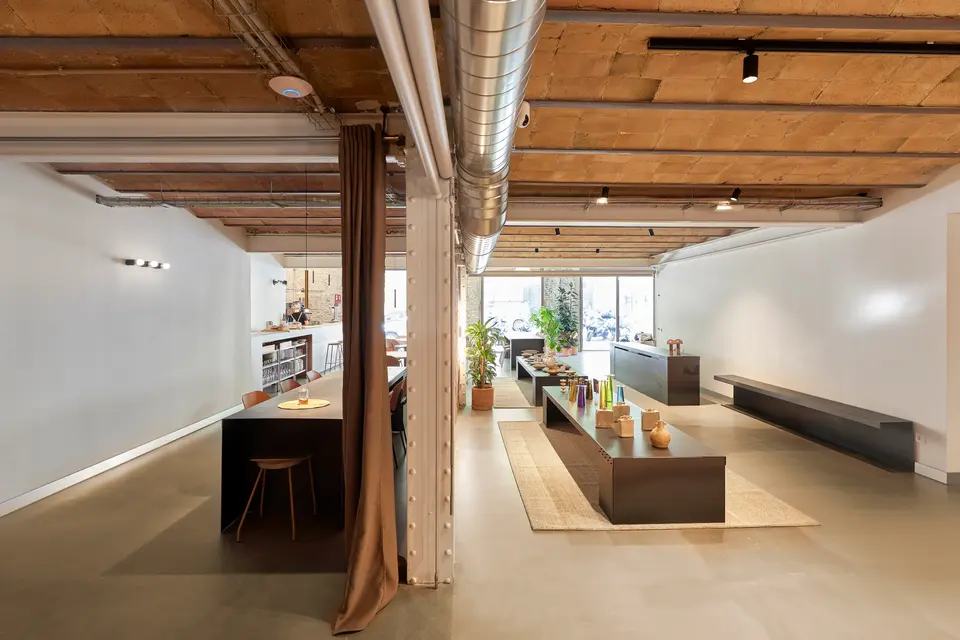 Long white-walled room with a brick ceiling, a low display table on a rug and an open kitchen area at the back