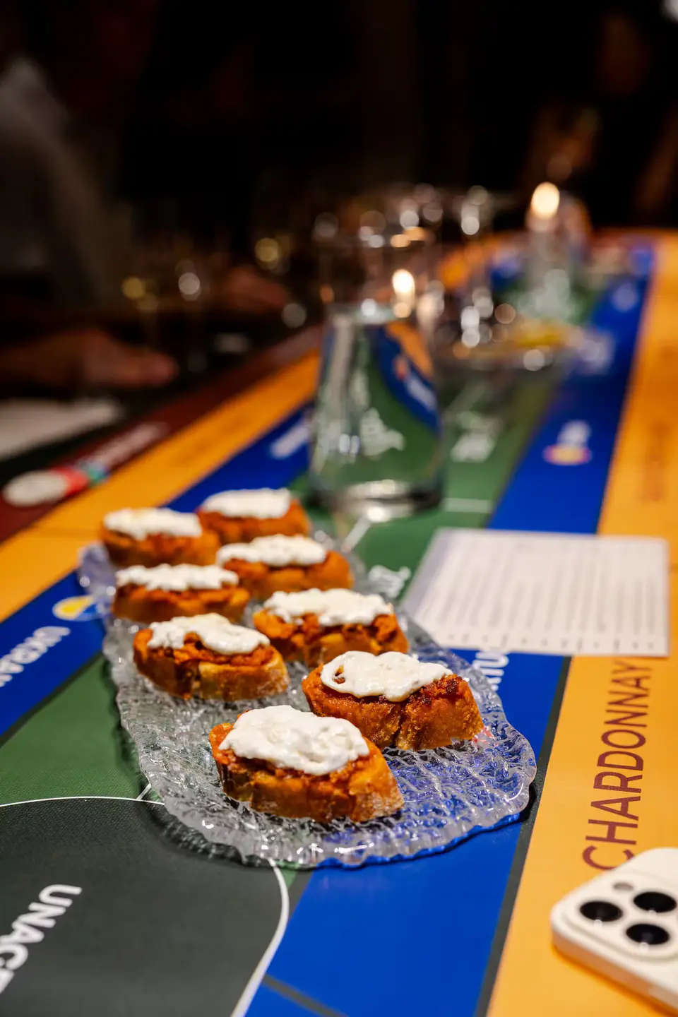 Glass dish of small buns with white icing on the game board, with candles and glasses blurred behind