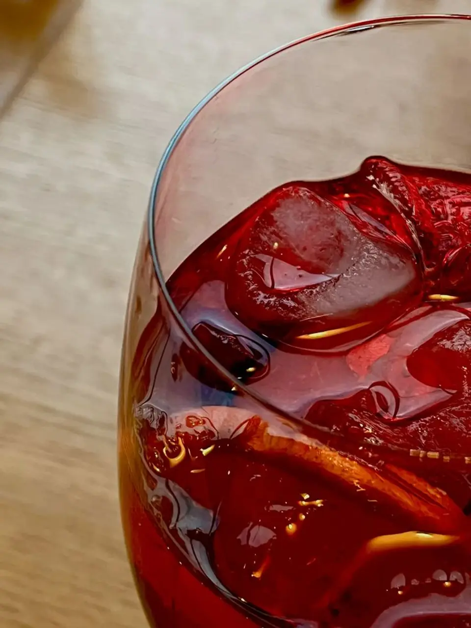 Close-up of a glass with a red drink, ice cubes and an orange slice on a wooden table