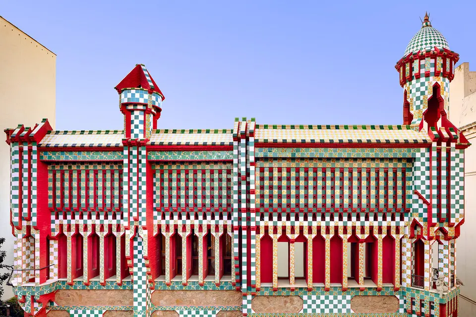 Green and white tiled façade with red panels and two turrets under a clear blue sky