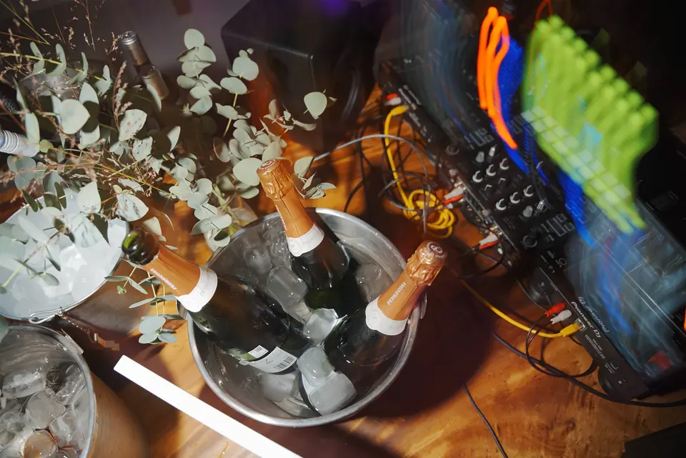 Ice bucket with sparkling wine bottles beside audio equipment with cables and eucalyptus branches