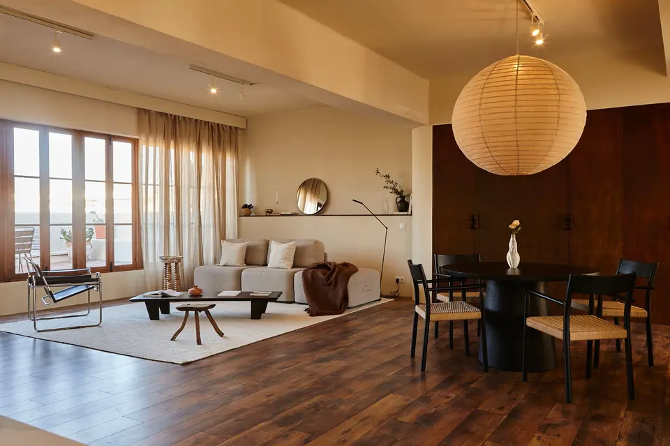 Lounge area with a grey sofa and low table, a round black dining table with woven-seat chairs and a large paper lamp