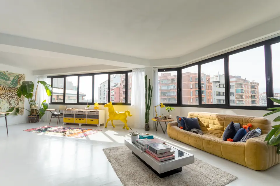 Bright living area with a white floor, a mustard yellow sofa, a metal coffee table, a yellow horse figure and black windows
