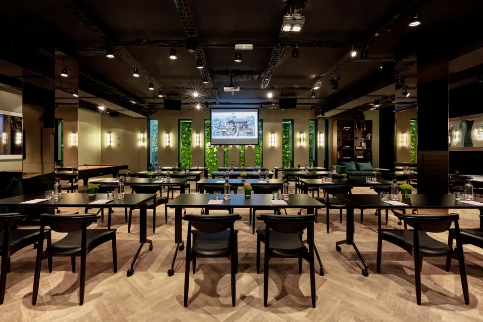 Classroom layout with black tables in rows and black leather chairs on a herringbone floor, with a screen and green walls