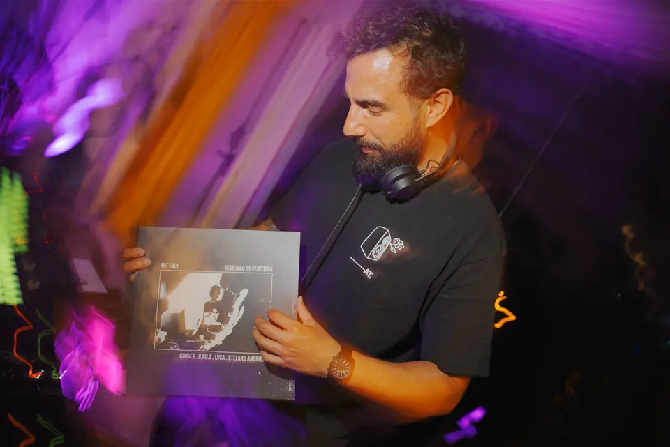 Person with headphones around the neck holding a vinyl record in its sleeve, surrounded by blurred colored lights