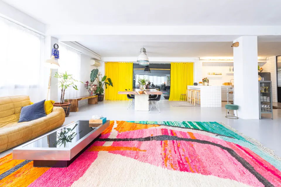 Pink, orange and turquoise rug in the foreground, with a yellow sofa on the left and yellow curtains at the back