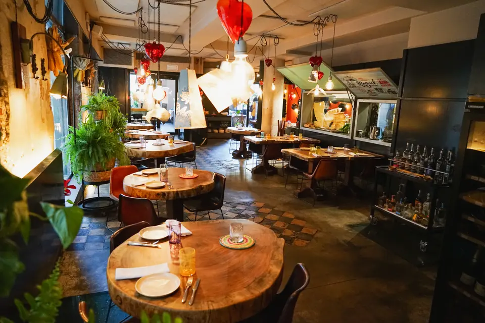 Dining room with round solid wood tables, hanging red lamps and plants, with a display case at the back