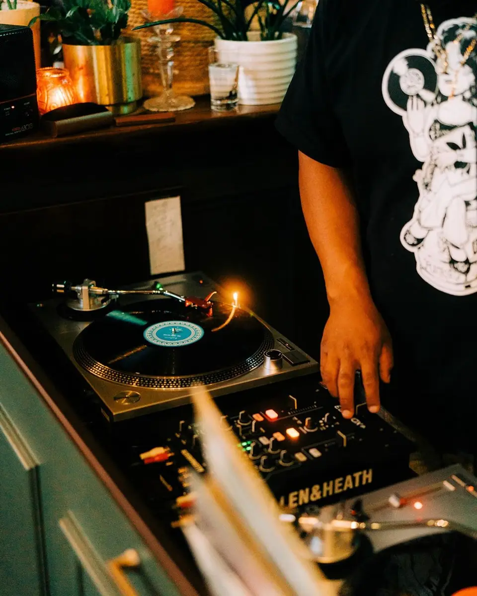 Turntable with a spinning record next to a mixer, operated by a person in a black T-shirt