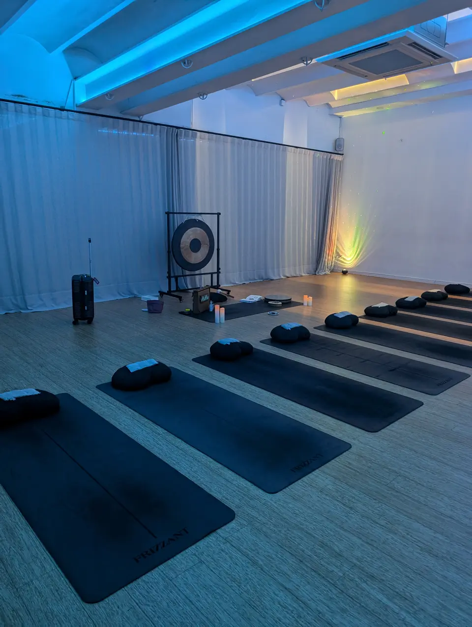Empty room with black mats and cushions in a row, a gong at the back and white curtains under blue light