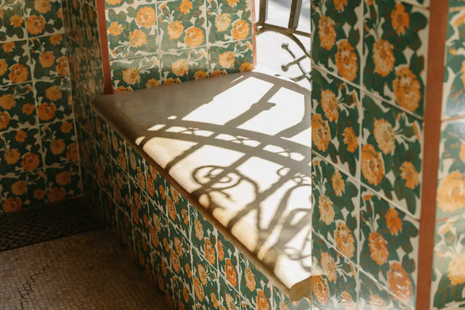 Stone seat by a window, with walls of orange flower tiles and the shadow of wrought ironwork