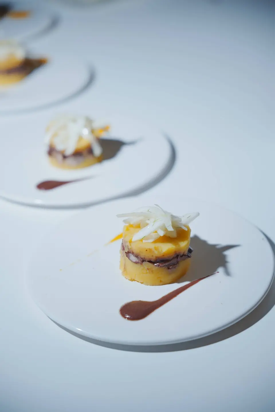 Three white plates in a row, each with a small yellow portion with a dark layer, pale strips on top and a streak of red sauce