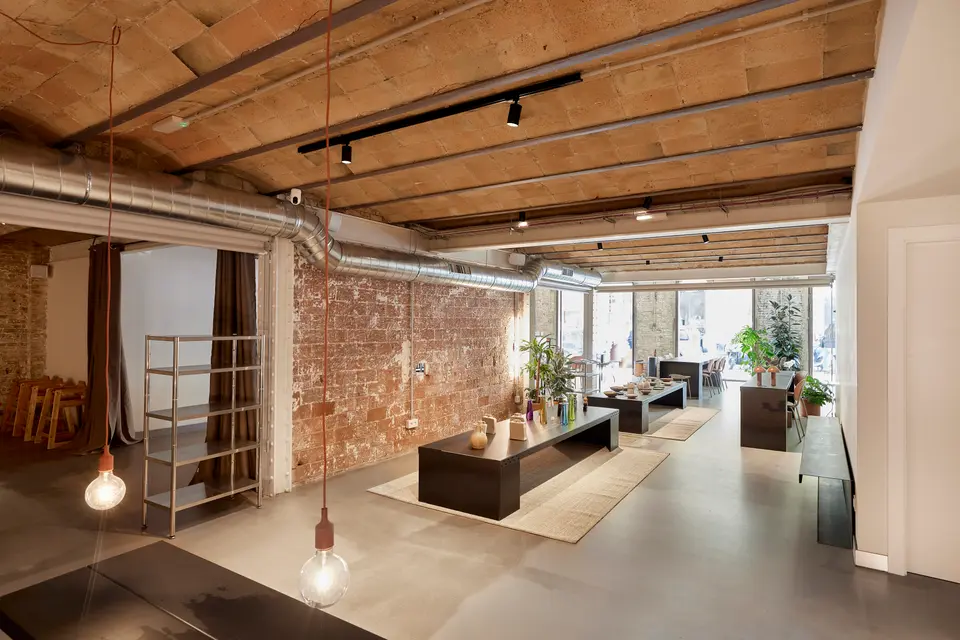 Floor with a vaulted brick ceiling and ventilation duct, with low black tables displaying objects and hanging bulbs