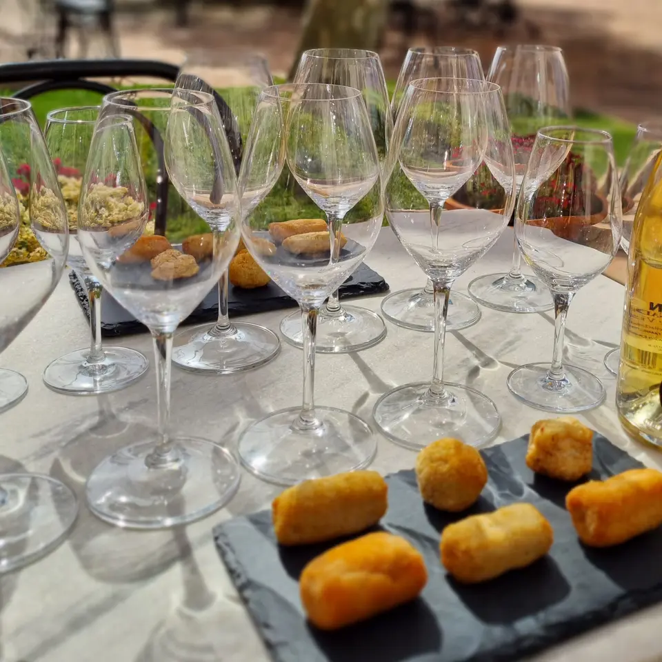 Golden croquettes on a slate board, with empty wine glasses lined up on an outdoor table