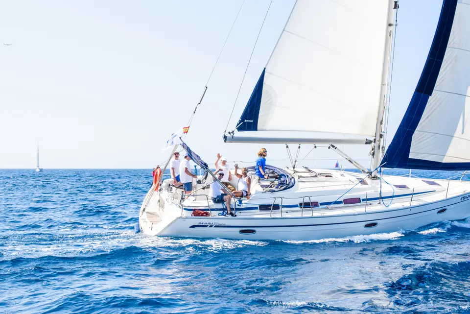 White sailboat with sails set on blue water, the crew at the stern raising their arms