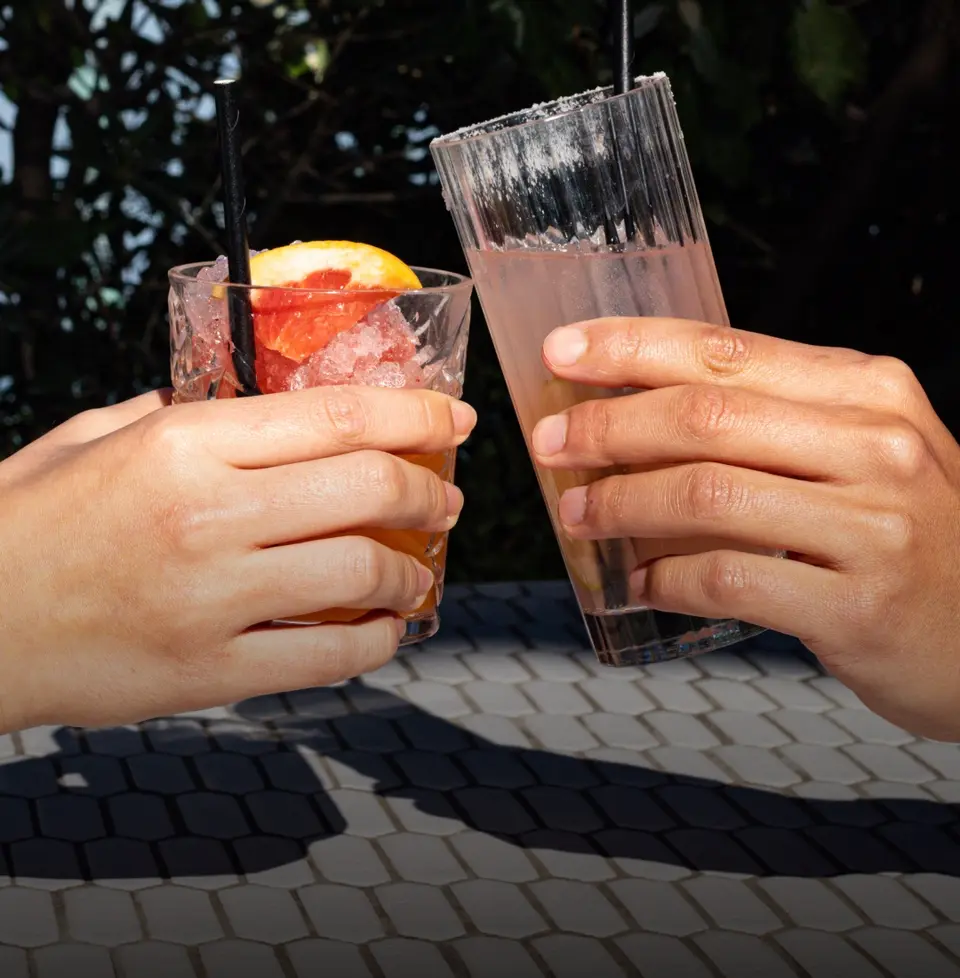 Two people toasting with cocktails on a sunny terrace