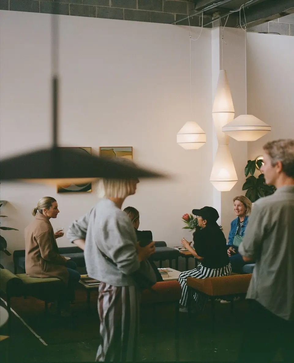 People standing and seated in conversation in a lounge with sofas, hanging paper lamps and warm light