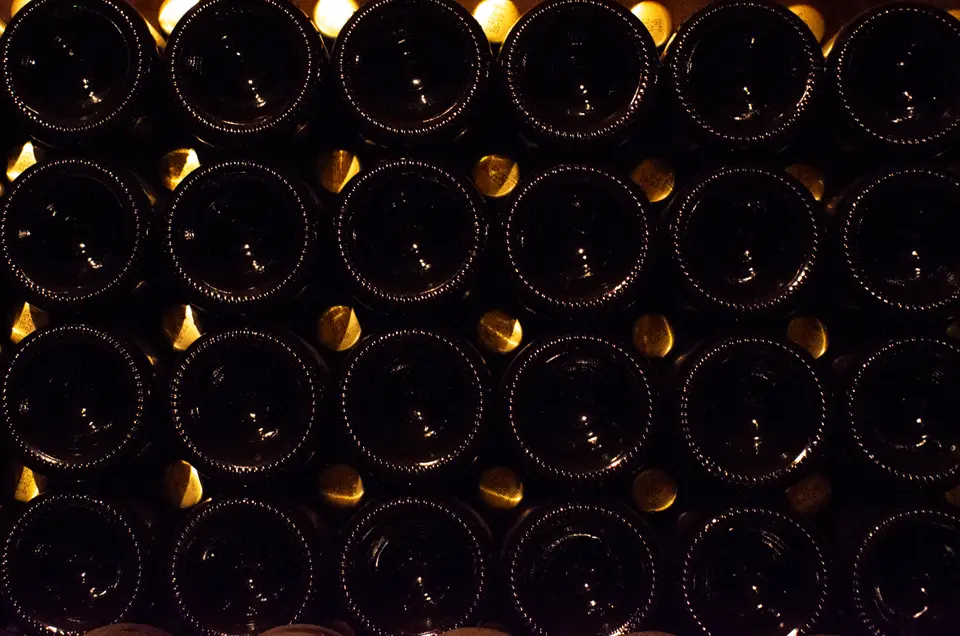 Wall of upside-down bottles in a dim cellar, with golden reflections between their bases