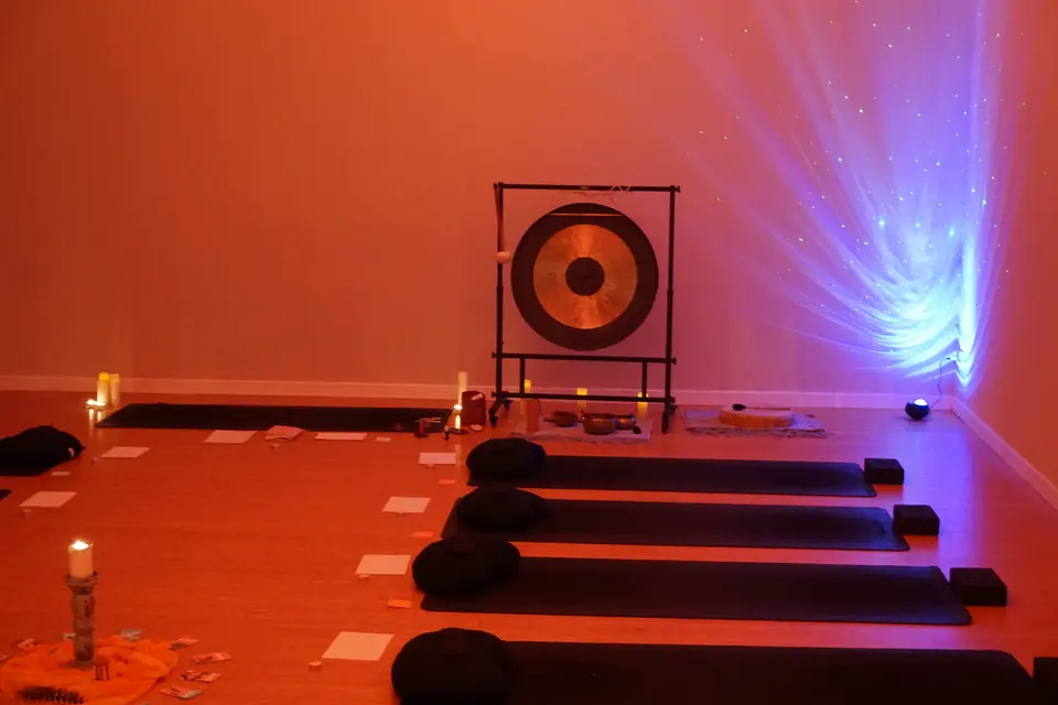 Yoga room with black mats, round cushions, candles and a gong, in reddish light with a blue projection on the wall