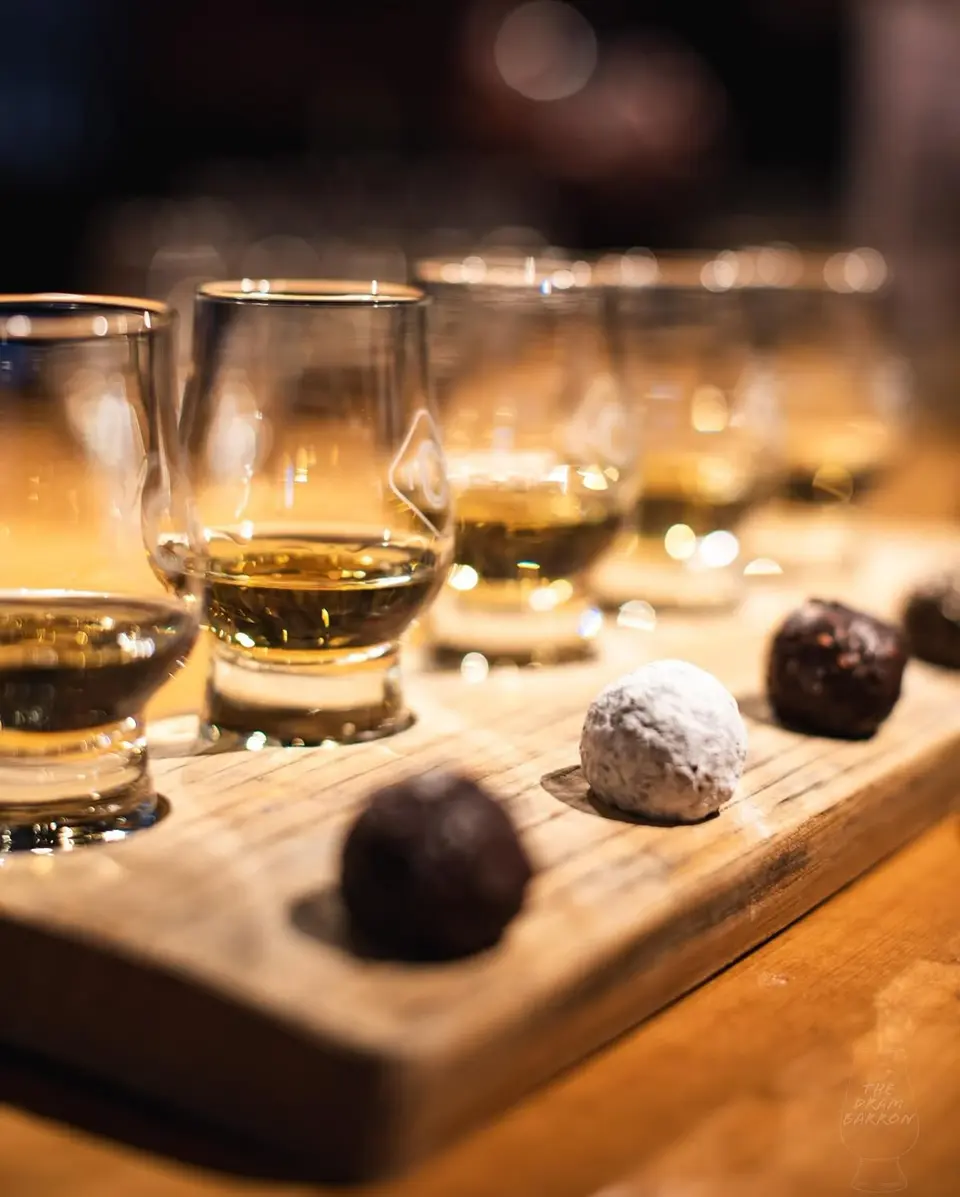Wooden board with whisky tasting glasses and three chocolate truffles in the foreground