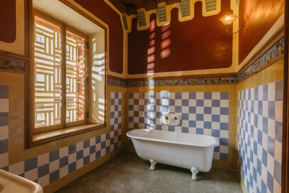 Bathroom with a white clawfoot tub, blue and yellow tiled walls and a lattice window filtering the light