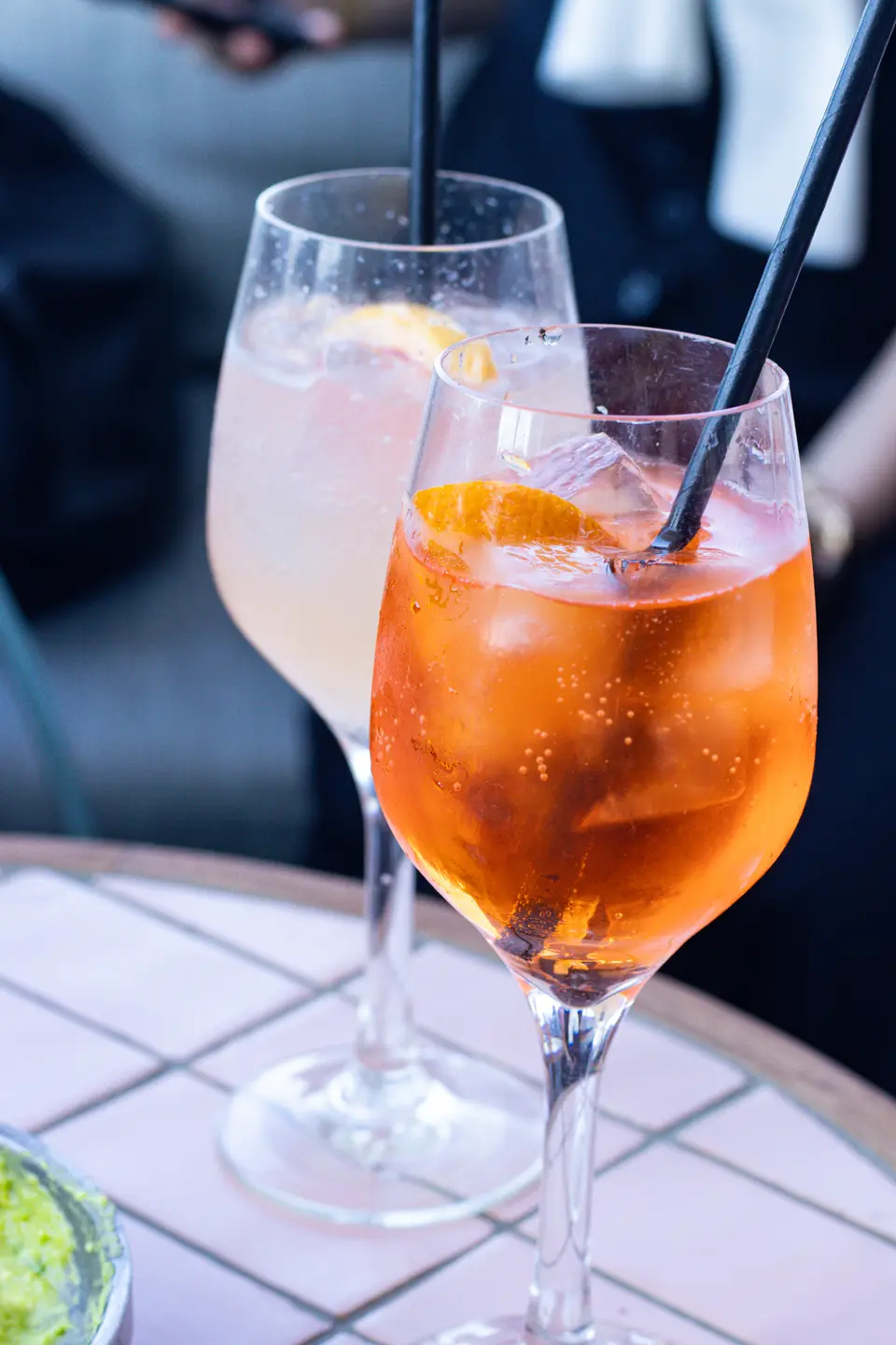 Two cocktail glasses with orange slices and black straws on a table, one orange and one paler