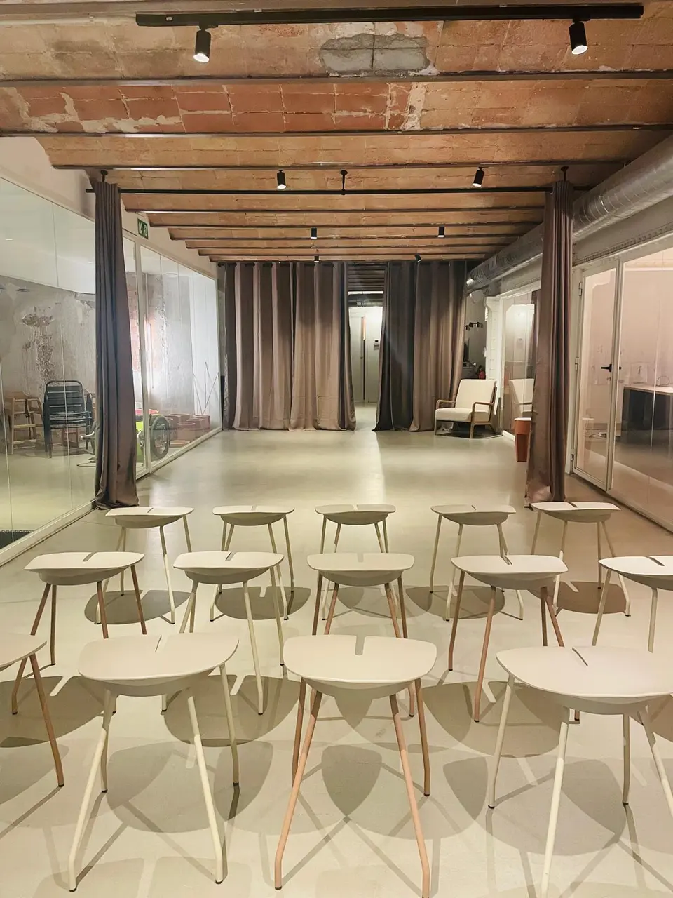 Rows of beige stools facing curtains at the far end of the room, with glass partitions on both sides and ceiling beams