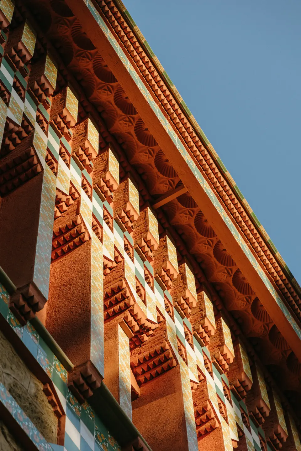 Rows of stepped terracotta brackets and green tiles under the eaves, in an oblique shot against a blue sky
